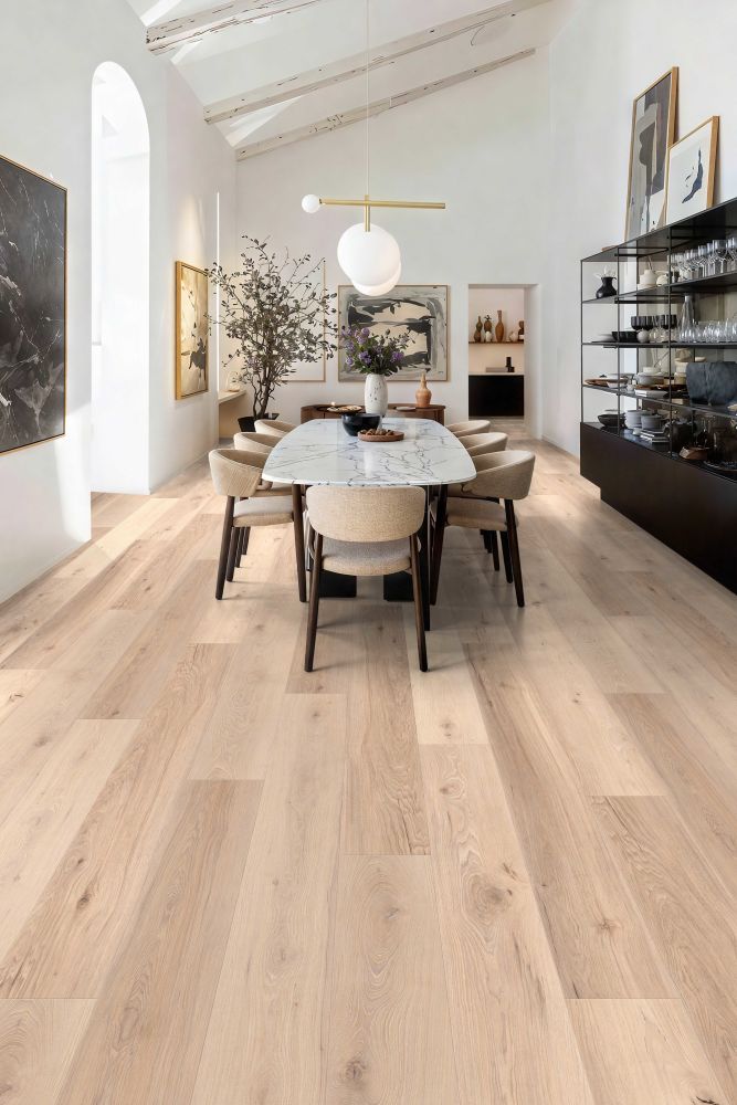 Bright dining room with a marble-topped table, beige chairs, and light wood flooring under white walls and exposed beams.
