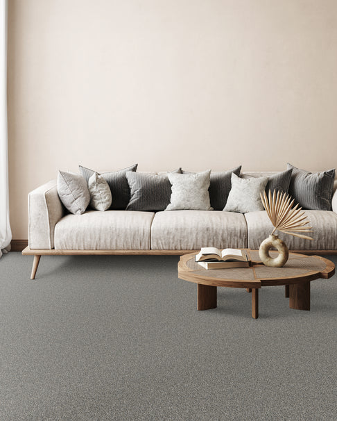 Beige sofa with gray and white cushions in a minimalist living room; round wooden coffee table with an open book and a decorative vase.
