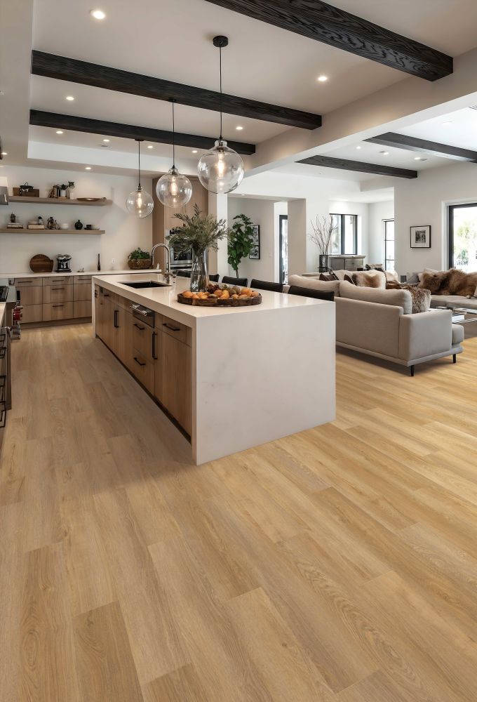 Bright open-plan kitchen with a white island, glass pendant lights, and a living area with beige sofas in the background.
