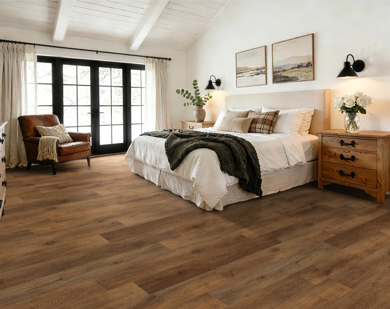 Bright bedroom with a large white bed, wooden nightstands, and a leather armchair by French doors.