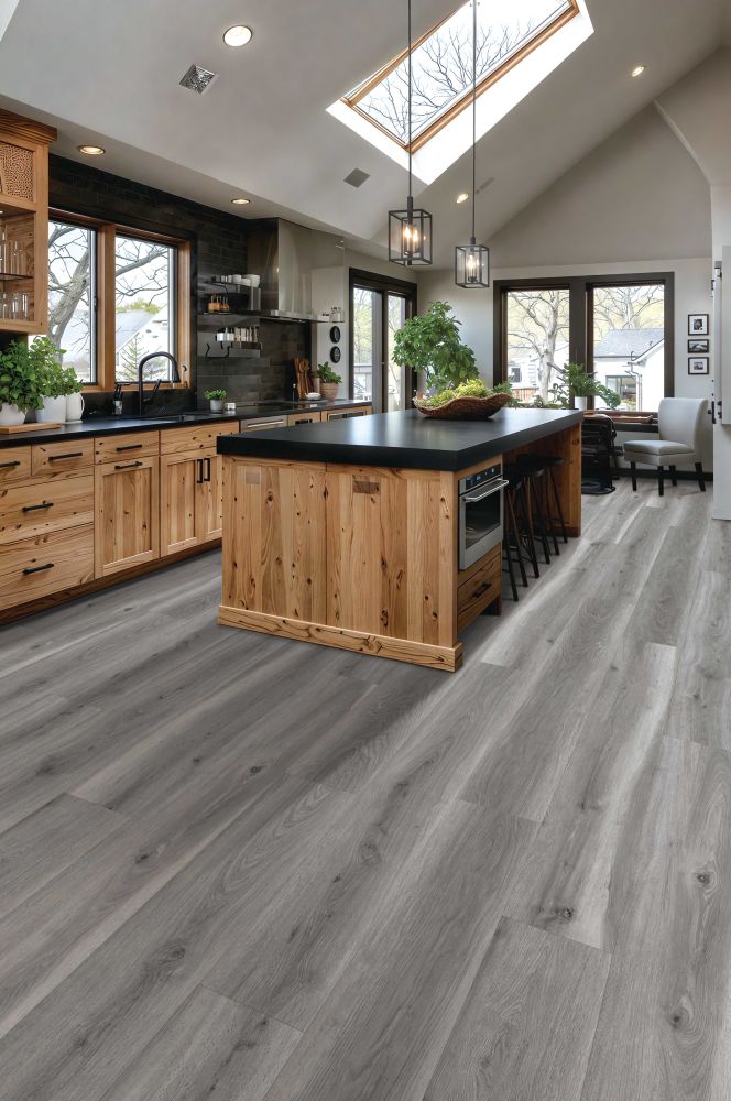 Modern kitchen with wooden cabinets and a central island topped by a dark countertop under skylights and windows in a bright space.