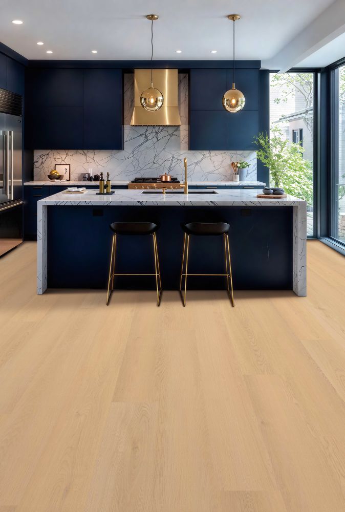 Modern navy kitchen with a marble island and two black stools with gold legs, gold faucet, and marble backsplash under pendant lights.