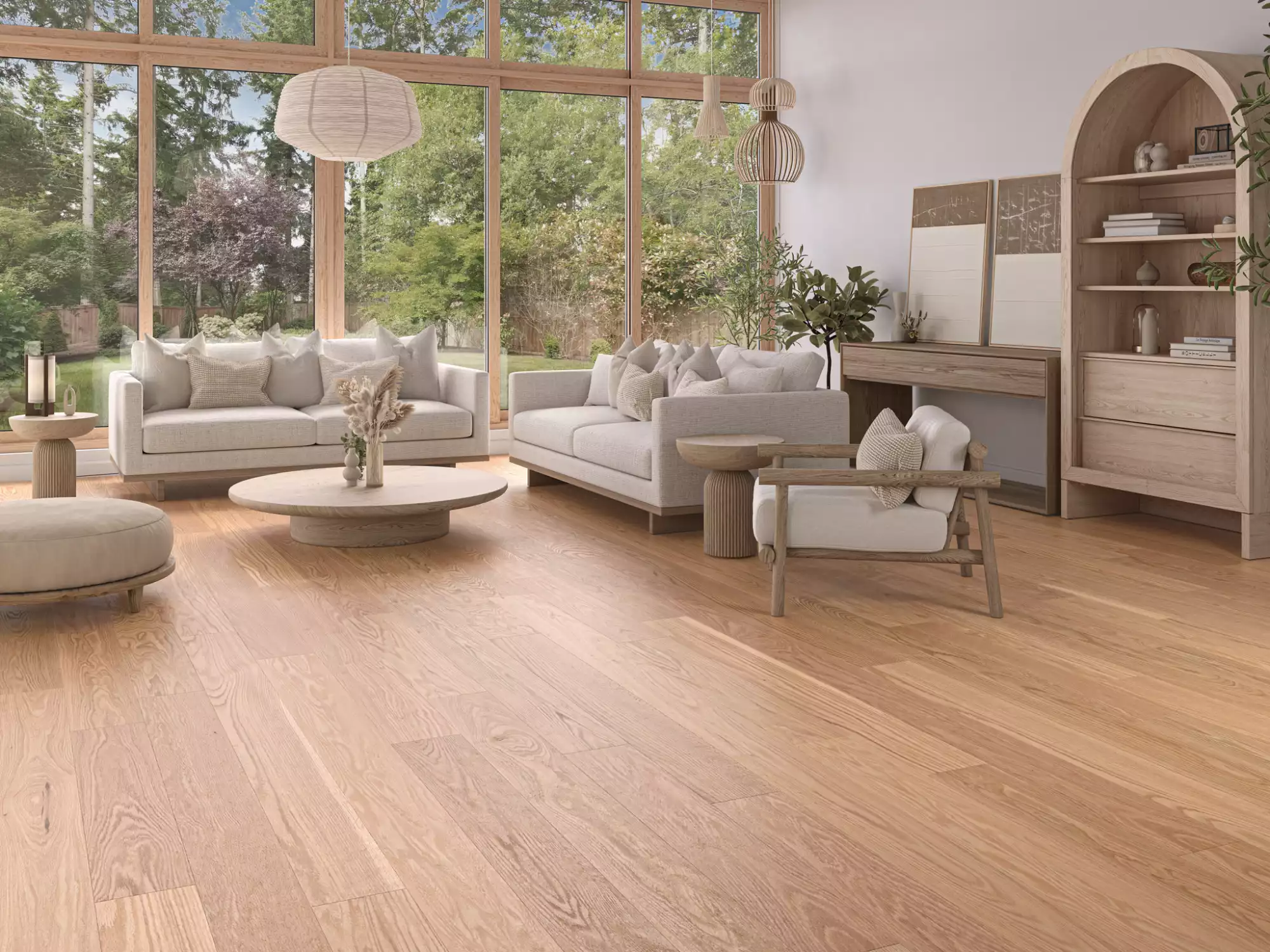 Bright living room with large glass windows, beige sofas, and light wood furniture; greenery visible outside.